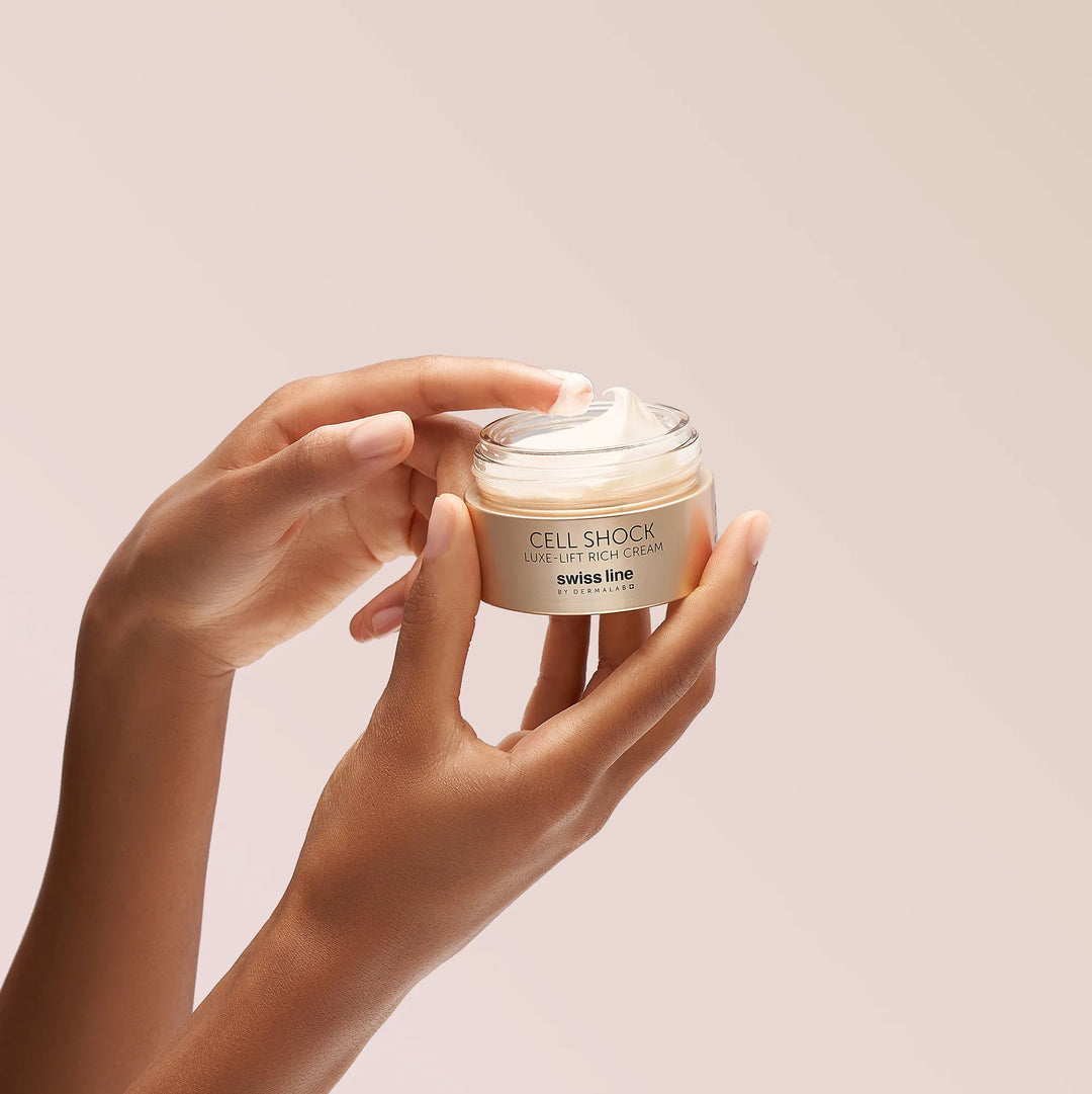 Hand holding a jar of 'Cell Shock' cream against a light pink background