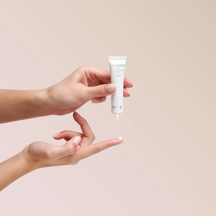 Hand holding a small white tube of skincare product against a beige background