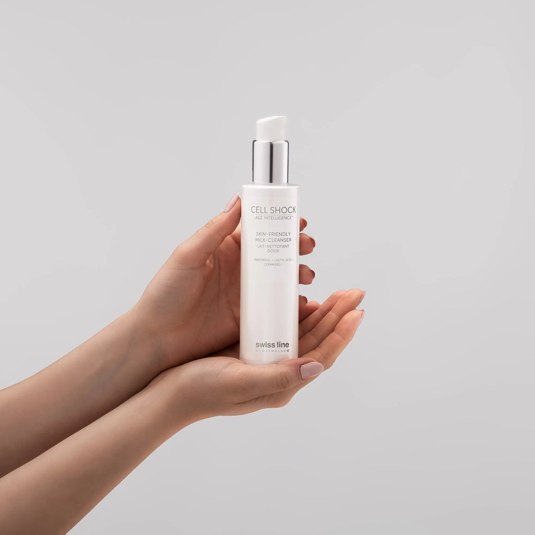 Hand holding a skincare bottle labeled 'Milk Cleanser' against a plain background