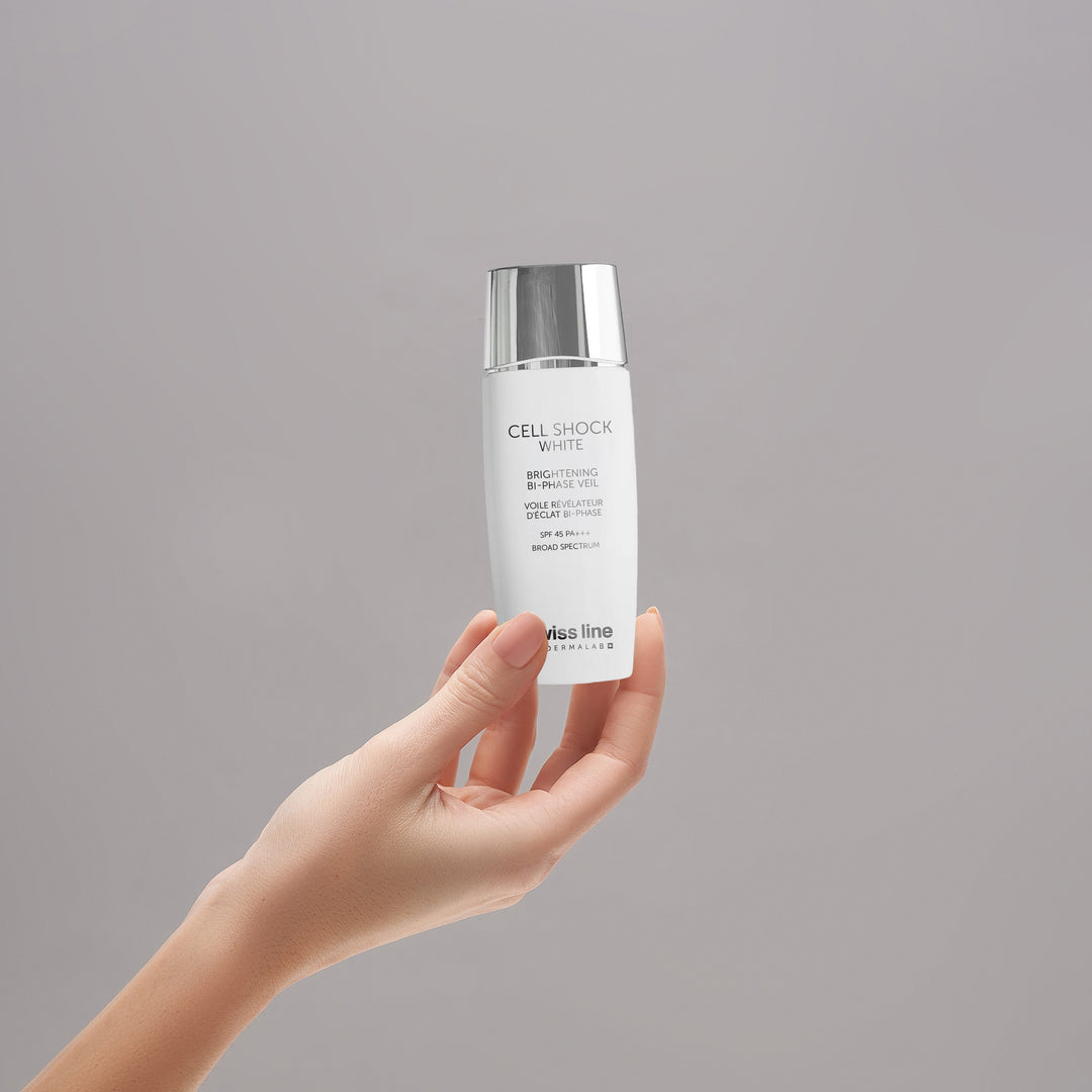A hand holding a white bottle of Alza Line Cell Shock White Brightening Serum against a solid gray background.