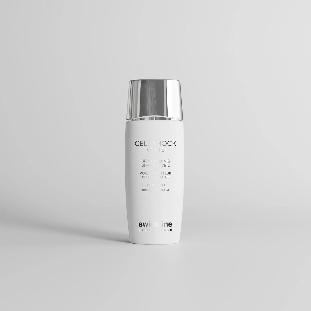 A white cylindrical skincare bottle with a reflective silver cap, standing upright on a light gray surface against a neutral light gray background. The label reads 'Cell Shock White' and 'swissline by design'.