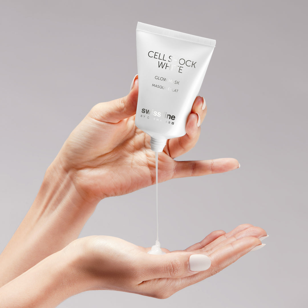 A person's hands holding a white squeeze tube of Swiss Cell White Glow Mask Hair against a solid gray background, with the white gel mask being dispensed onto the palm.