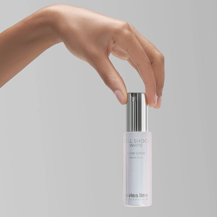 A hand holding the cap of a Swiss Line Cell Shock White glow serum bottle against a solid gray background.