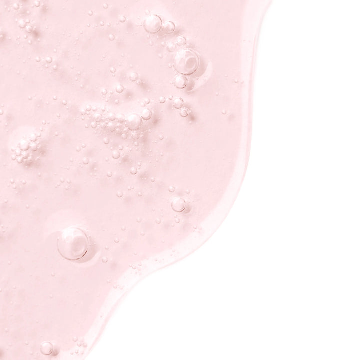 A close-up of a translucent light pink liquid with small bubbles, positioned on the left side of a clean white background.