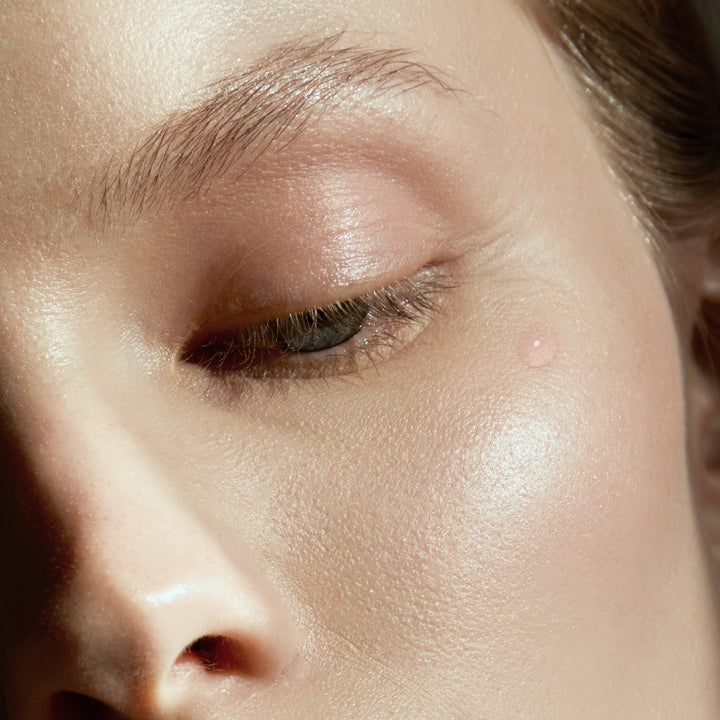 Extreme close-up of a person's eye and surrounding face with warm, shimmery skin and soft lighting.