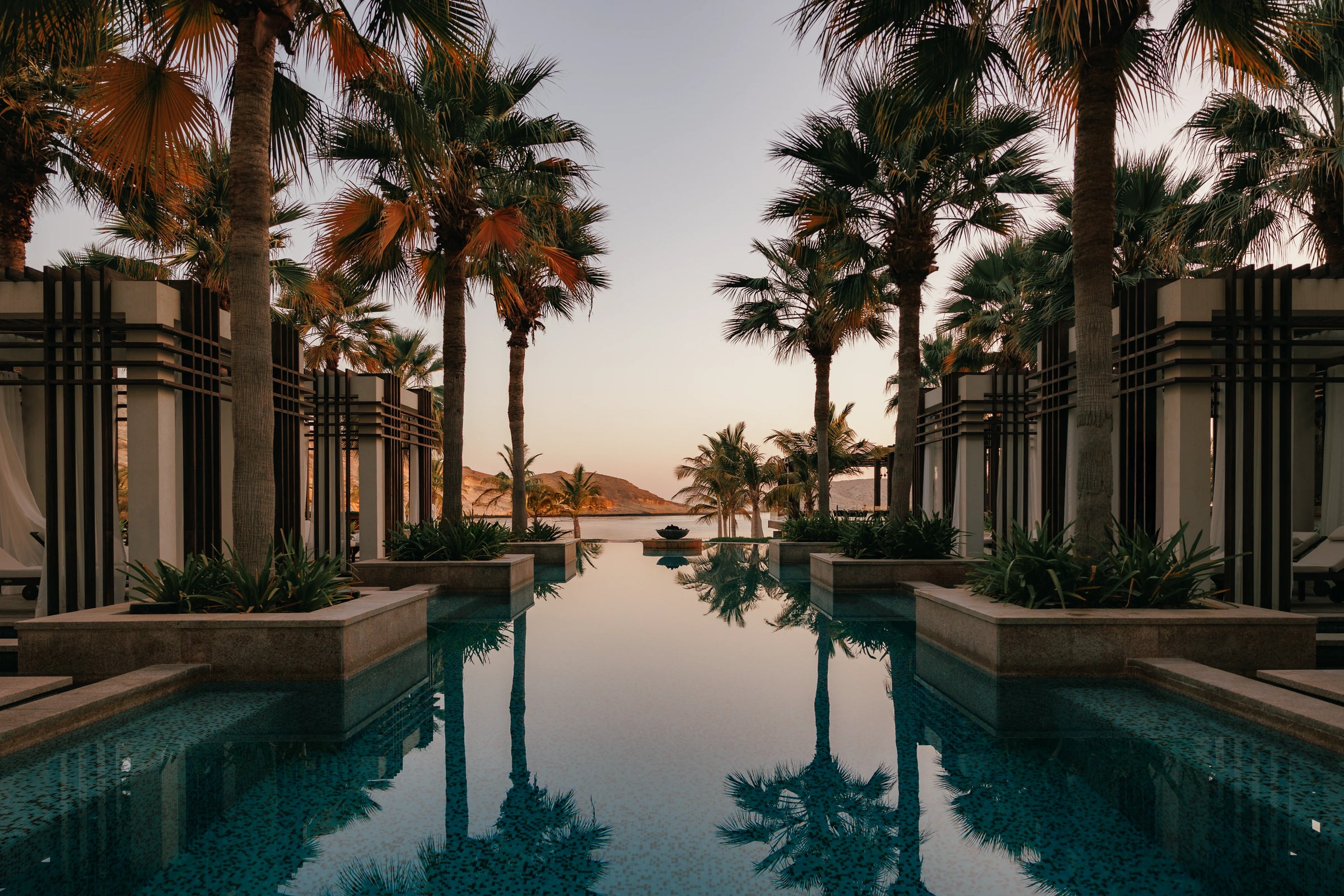 Pool area with palm trees and modern architecture during sunset.