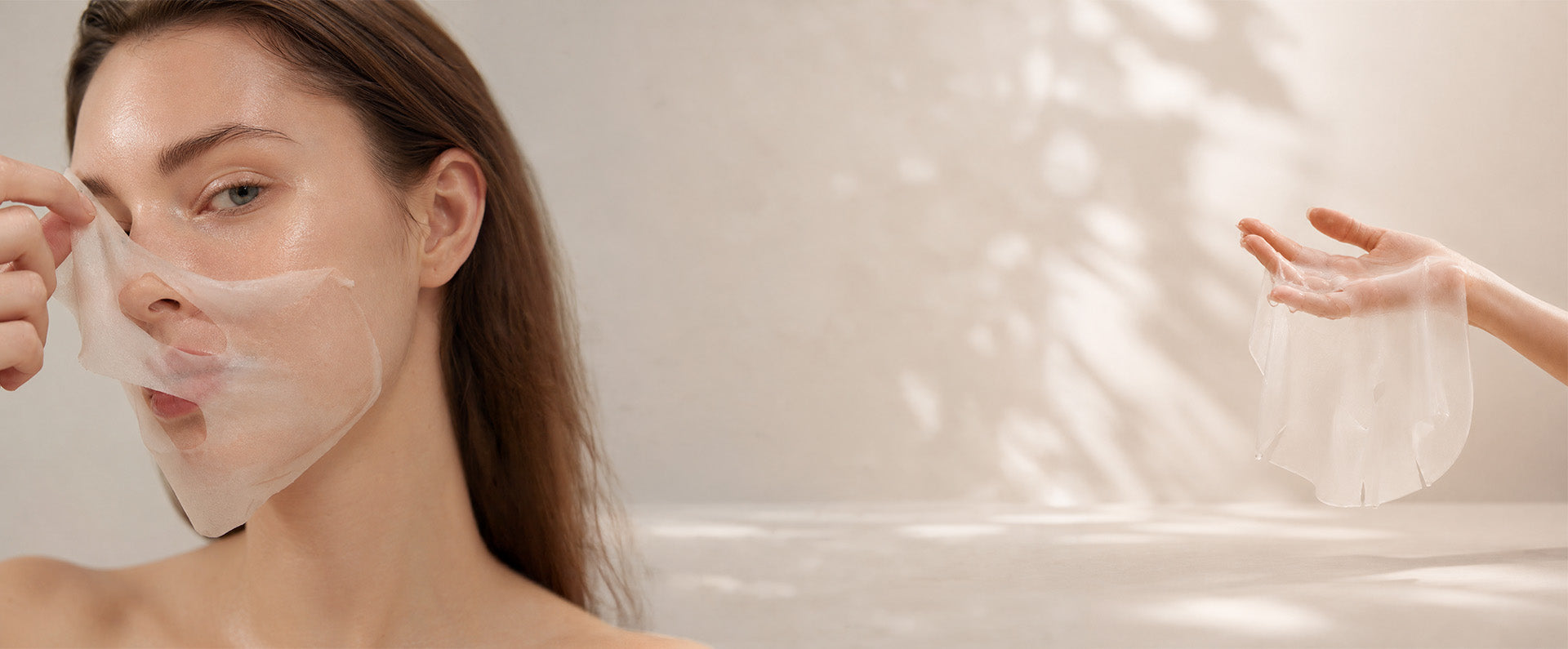 A woman is shown wearing a translucent white sheet mask on her face, with another hand holding a matching sheet mask to the right. The background is a soft, warm beige with dappled light shadows.
